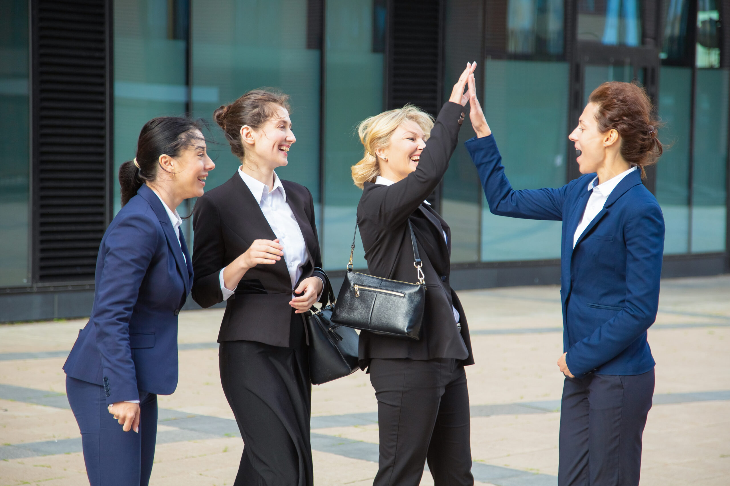 Happy excited business ladies giving high five. Businesswomen wearing suits meeting in city, celebrating success. Team success and teamwork concept